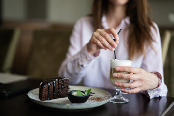 Close up hands woman sit in coffee shop cafe restaurant indoors hold latte, chocolate brownie dessert cake.