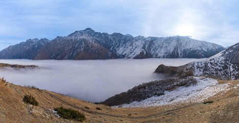 Fototapeta na wymiar Panorama view of the stunning Caucasus mountains with sea of mist. Beautiful mountain view of the snow-capped peaks near Stepantsminda, Georgia.
