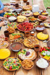 Homemade Romanian Food with grilled meat, polenta and vegetables Platter on camping. Top view of group of people having dinner together on wooden table in garden.