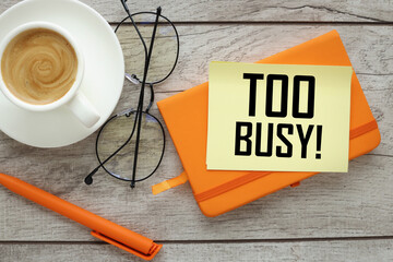 Too Busy. text on a yellow note and a table with an orange notepad. - obrazy, fototapety, plakaty