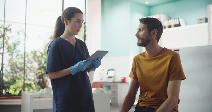 Caucasian Man Sitting In The Chair In Bright Hospital And Listening To Female Nurse With Tablet Computer. Professional Woman Explaining Possible Side Effects After Vaccination Or Medicine Injection.