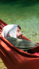 Hombre con capucha durmiendo en hamaca a la orilla de un río