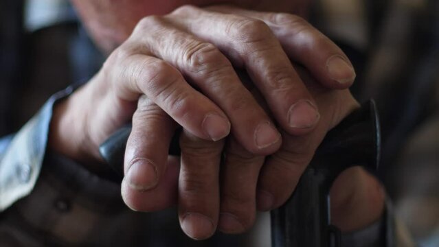 close-up of an elderly man put his hands on a walking stick and lowered his head, the concept of depression, despair, loneliness in old age