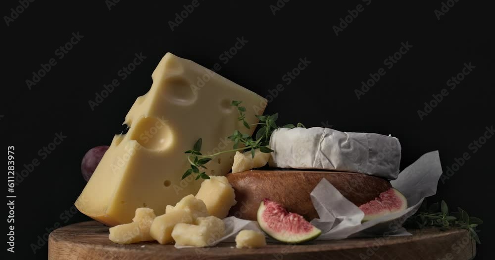 Poster still life with various cheese on wooden cutting board rotating on black background