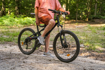 Fototapeta premium Senior man standing with bicycle in the grassy park at the summer