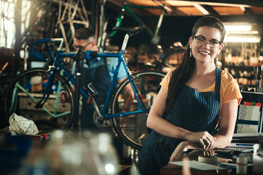 Portrait, mechanic and smile of woman in bicycle shop, repair store or cycling workshop. Face, bike technician and confident female person, business owner and professional standing with glasses.