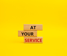 At your service symbol. Wooden blocks with words At your service. Beautiful yellow background. Business and At your service concept. Copy space.