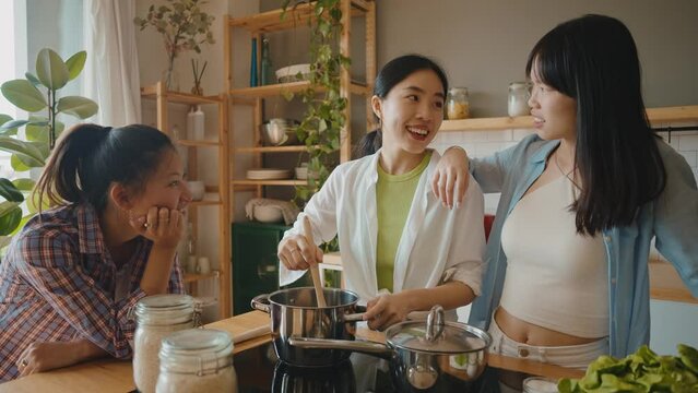 Three happy young women preparing asian food in the kitchen. Group of female friends enjoying their girls day at home cooking an healthy meal with vegetables and organic ingredients. lifestyle concept