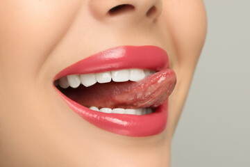 Woman showing her tongue on light background, closeup