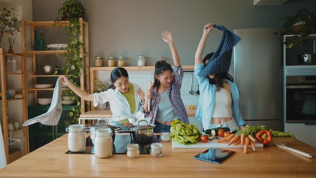 Three happy young women preparing asian food in the kitchen. Group of female friends enjoying their girls day at home cooking an healthy meal with vegetables and organic ingredients. lifestyle concept