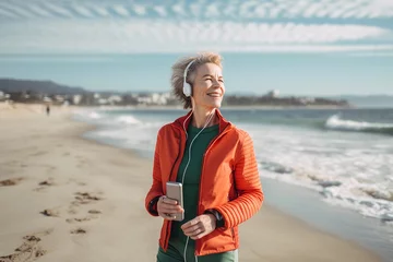 Foto op Aluminium Smiling mature woman in green jacket and red jacket on the beach with her mobile phone and headphones listening to music image ai generate © Creative Clicks