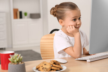 Little girl using computer at table in room. Internet addiction