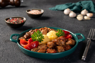 Delicious romanian food pomana porcului made from chunks of fried pork and sausages served with mamaliga and pickled red peppers close-up in a plate on dark background. Horizontal