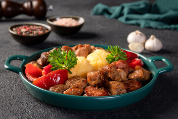 Romanian festive dish pomana porcului consisting of pieces of fried pork and sausages with pickled red peppers and polenta close-up on a plate on dark background. Horizontal.