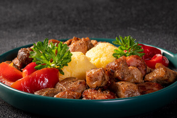 Romanian festive dish pomana porcului consisting of pieces of fried pork and sausages served with polenta and pickled red peppers close-up on a plate. Horizontal.