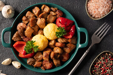 Romanian festive dish pomana porcului consisting of pieces of fried pork and sausages with pickled red peppers and corn porridge on a plate on the table. Horizontal top view.