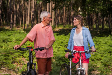 Senior father and his daughter looking at each other while walking with bikes at the forest
