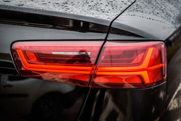 Car tail light. Detail black metallic car with rear light close up. Rear lamp signals for turning car on street. Right back modern headlight car. Signal function to keep them distance. Trunk closeup.