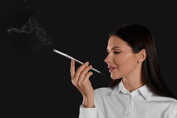 Obraz premium Woman using long cigarette holder for smoking on black background, space for text