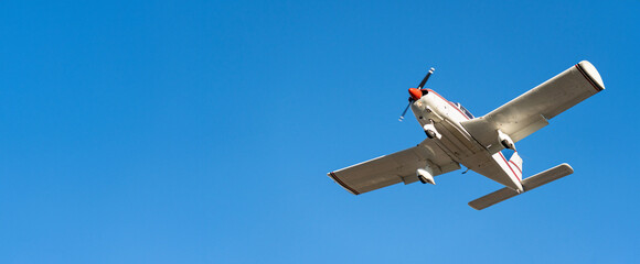 Small white cessna single propeller plane flying in a clear blue sky maneuvering before landing at...