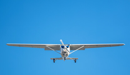 Small white plane with blue stripes of a cessna propeller flying in a clear sky before landing on Sabadell Airport