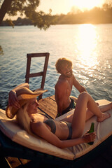 A young couple in swimsuit chatting while enjoying the sunset on the river bank. Summer, river, vacation