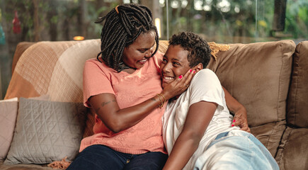 Mãe Brasileira negra fazendo carinho no seu filho no sofá da sala no dia das mães