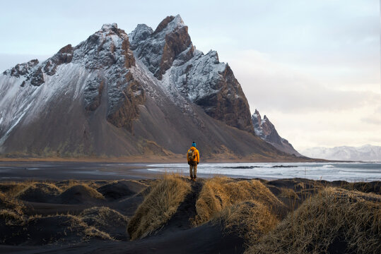 A tourist  stands on the beach, admiring the majestic reflection of the Vestrahorn mountain at Cape Stokksnes, Iceland, as the sun rises on the horizon. The beautiful snow-capped mountains.