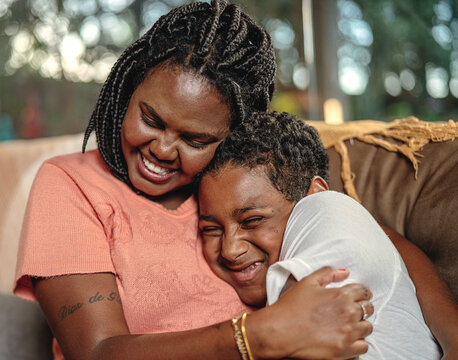 Mãe negra abraçando seu filho no sofá da sala no dia das mães no Brasil