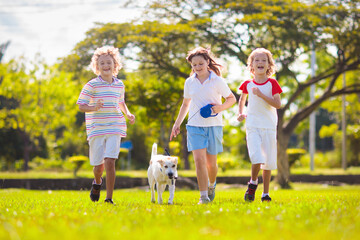 Fototapeta premium Kids play with dog. Children and puppy run in park