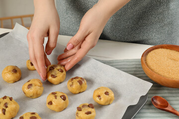 Woman preparing chocolate chip cookies at white table in kitchen, closeup