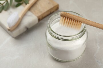 Bamboo toothbrush and jar of baking soda on light grey marble table