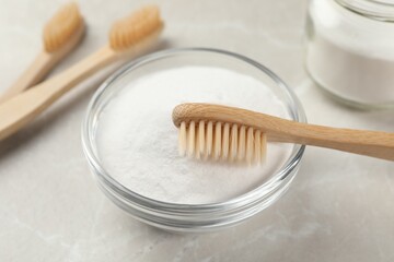 Bamboo toothbrush and glass bowl of baking soda on light table, closeup
