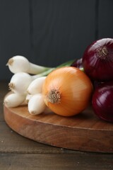 Board with different kinds of onions on wooden table, closeup
