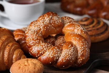 Freshly baked round braided bread and other pastries on wooden board, closeup