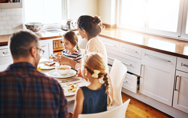 Family, morning and breakfast by table in kitchen for meal, eating or bonding time together at home. Mother, father and children with healthy food to start the day for nutrition or cereal in house