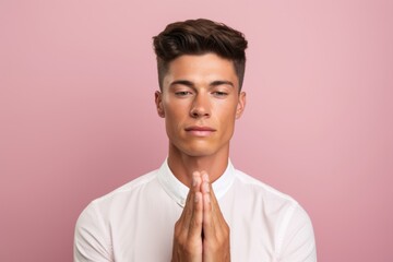 Headshot portrait photography of a glad boy in his 20s putting hands together as if praying against a pastel pink background. With generative AI technology