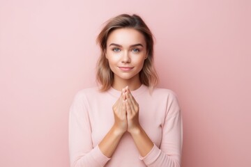 Medium shot portrait photography of a satisfied girl in her 20s making a sorry gesture with hands together against a pastel pink background. With generative AI technology