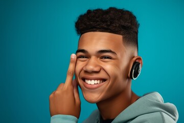 Fototapeta premium Headshot portrait photography of a happy boy in his 20s making a i'm listening gesture with the hand on the ear against a turquoise blue background. With generative AI technology
