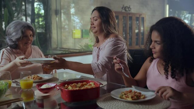 brazilian woman sitting at the table and having dinner serving food to her mother and her daughter during mother's day lunch