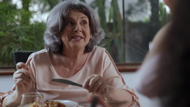Brazilian elderly grandmother sitting at the dining table eating and talking with her daughter during mother's day lunch