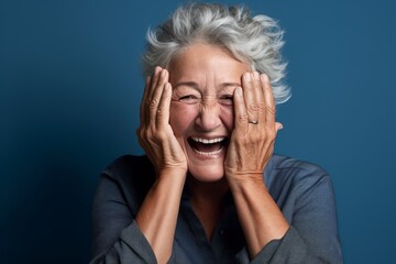 Headshot portrait photography of a happy mature woman putting hands on the face in a gesture of terror against a soft blue background. With generative AI technology