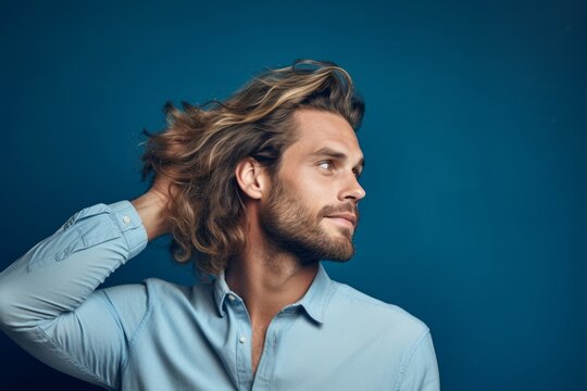 Medium shot portrait photography of a beautiful boy in his 30s touching her hair against a soft blue background. With generative AI technology