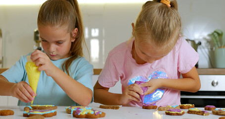 Little girls decorate cookies on table with icing Cooking treats for celebration