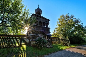 Belfry with arcades and onion shaped roof of wooden articular church in Hronsek which is part of wooden churches of Carpathian arch listed in UNESCO on summer day with blue sky and sun