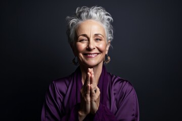Close-up portrait photography of a glad mature woman putting hands together as if praying against a deep purple background. With generative AI technology