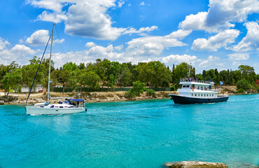 A Pleasure boat and a Yacht sail on the Corinth Canal in turquoise water. Summer landscape of the Corinth Canal in a bright sunny day against a blue sky with white clouds. Peloponnese, Greece