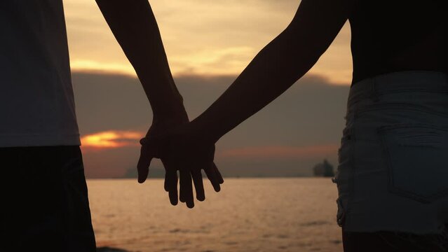 Close up man in love hesitantly holds out his hand, a woman takes his hand on a romantic date, on background of sunset on the sea. Concept of mutual sympathy is declaration of love.
