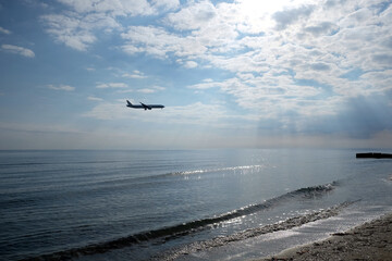 Fototapeta na wymiar Landscape with calm sea to horizon and big passenger aircraft preparing to landing