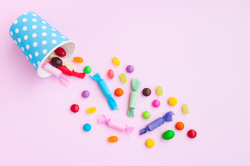 Different kinds of colorful candy out of a blue paper cup with white dot on pink background, Various candies